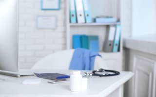 Biela ambulancia s fonendoskopom, liekmi, kalkulačkou a počítačom na stole.